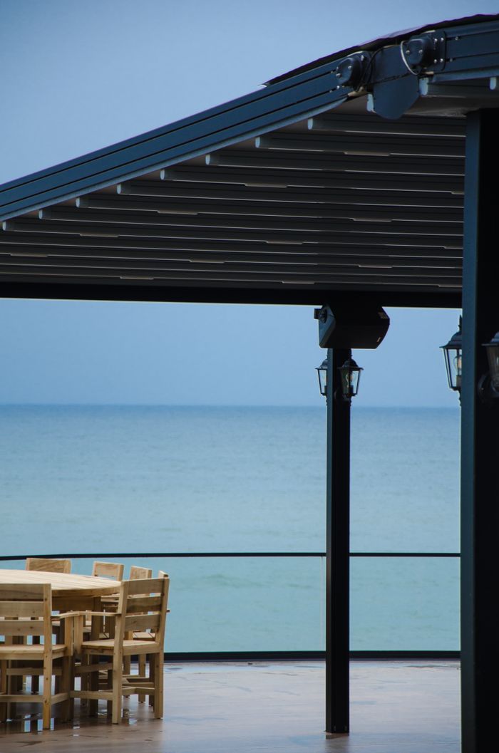 Serene ocean view from a patio with wooden chairs under a pergola. Ideal for relaxation.